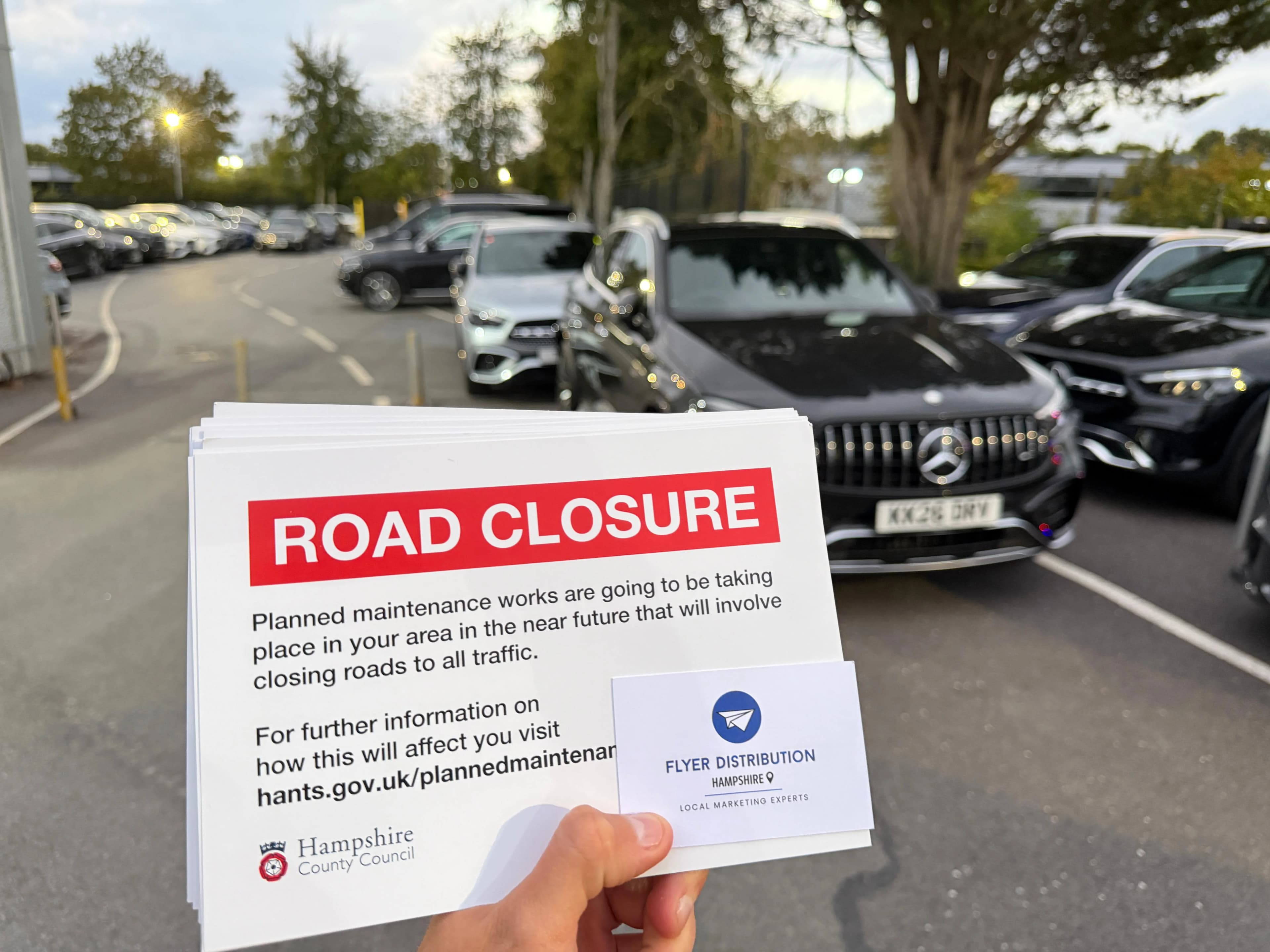 A stack of 'ROAD CLOSURE' public notice leaflets produced for Hampshire County Council, held alongside a Flyer Distribution Hampshire business card